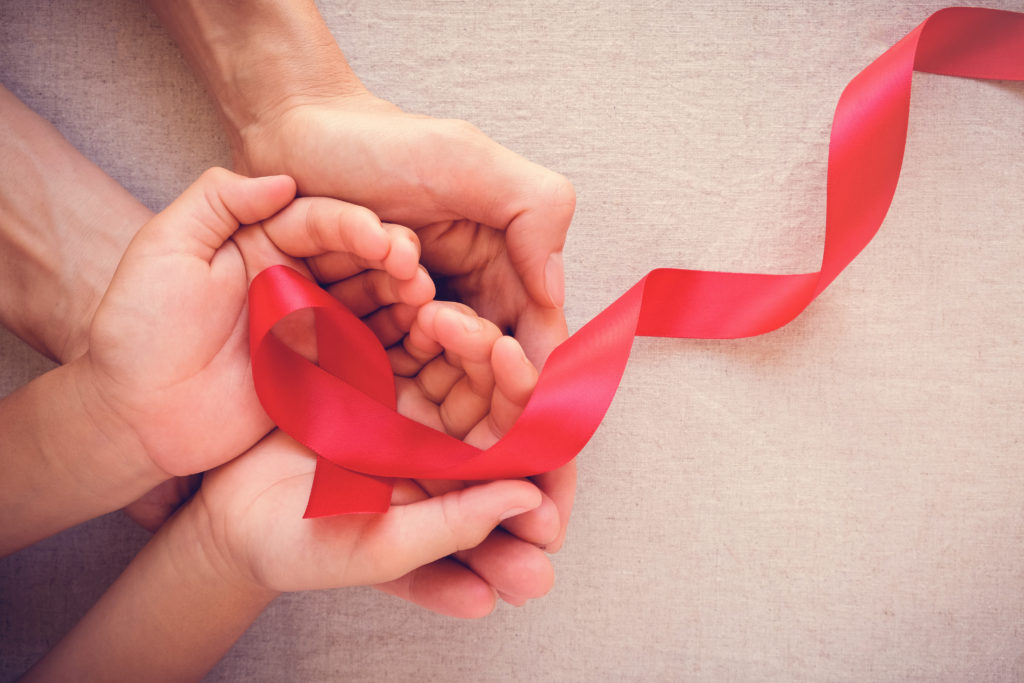 adult and child hands holding red ribbon, hiv awareness concept, world